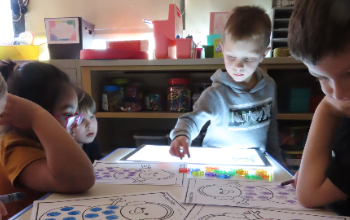 Kindergarten students engage with tabletop light panels during small group activity 